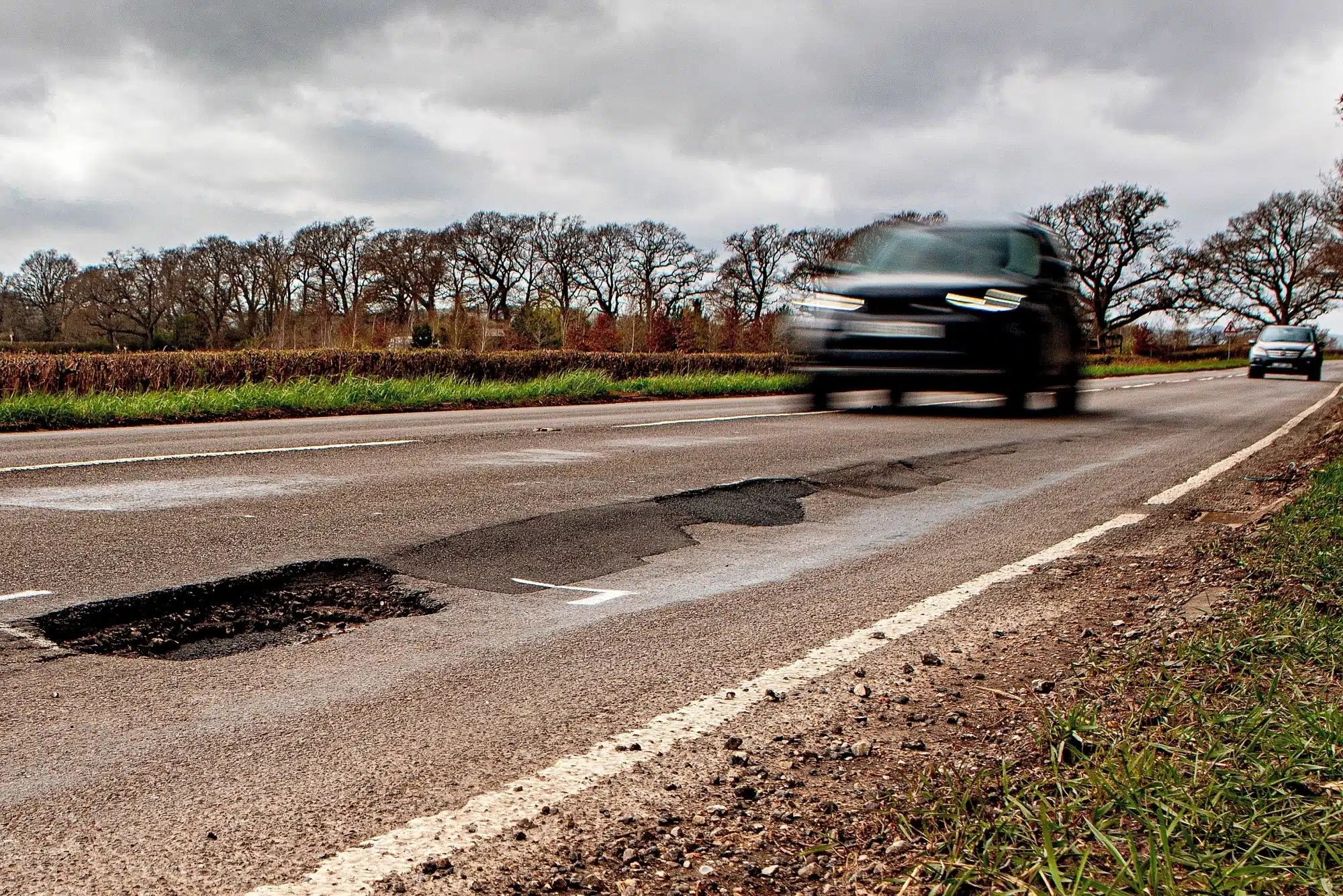 Blurred car approaching a deep, unmarked pothole